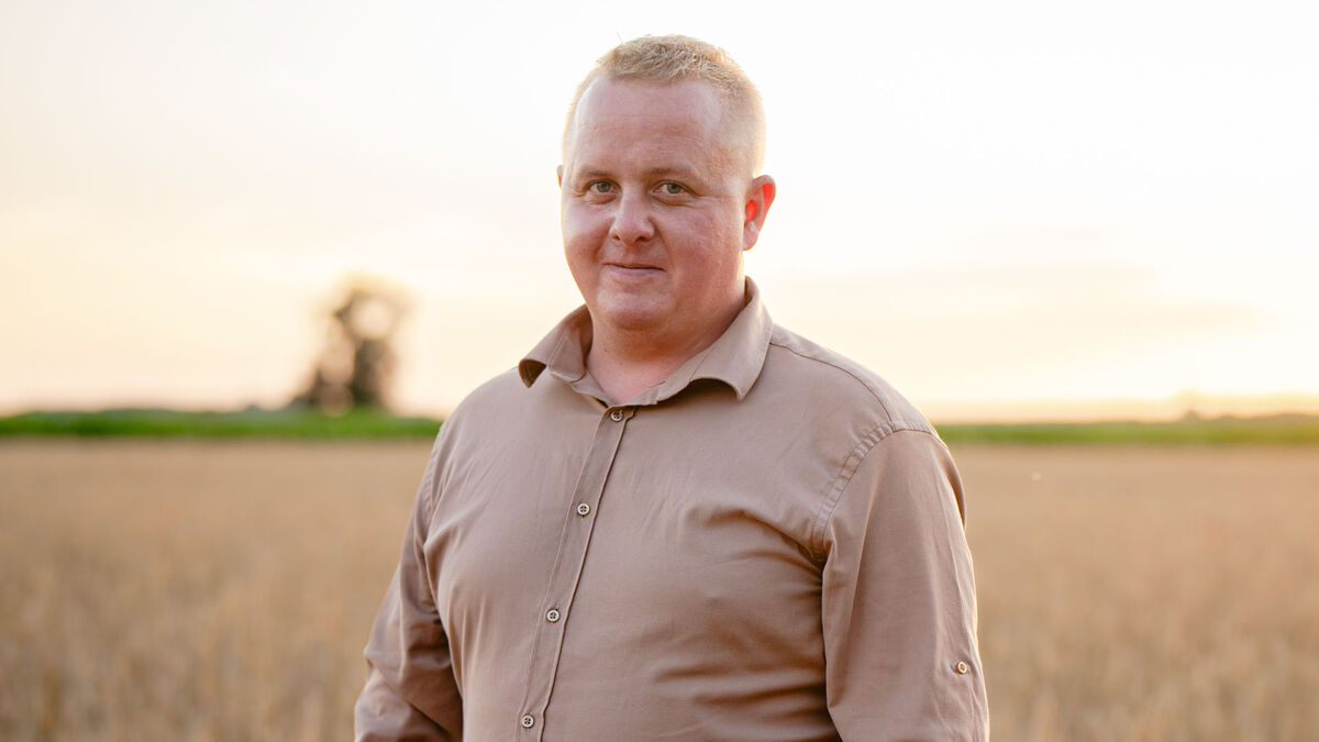 Wiktor z programu „Rolnik szuka żony” stoi na polu, ubrany w beżową koszulę. Mężczyzna jest zwrócony przodem i patrzy w stronę aparatu. W tle rozciąga się pole oraz jasne niebo, a w oddali widać zieleń i sylwetkę drzewa.