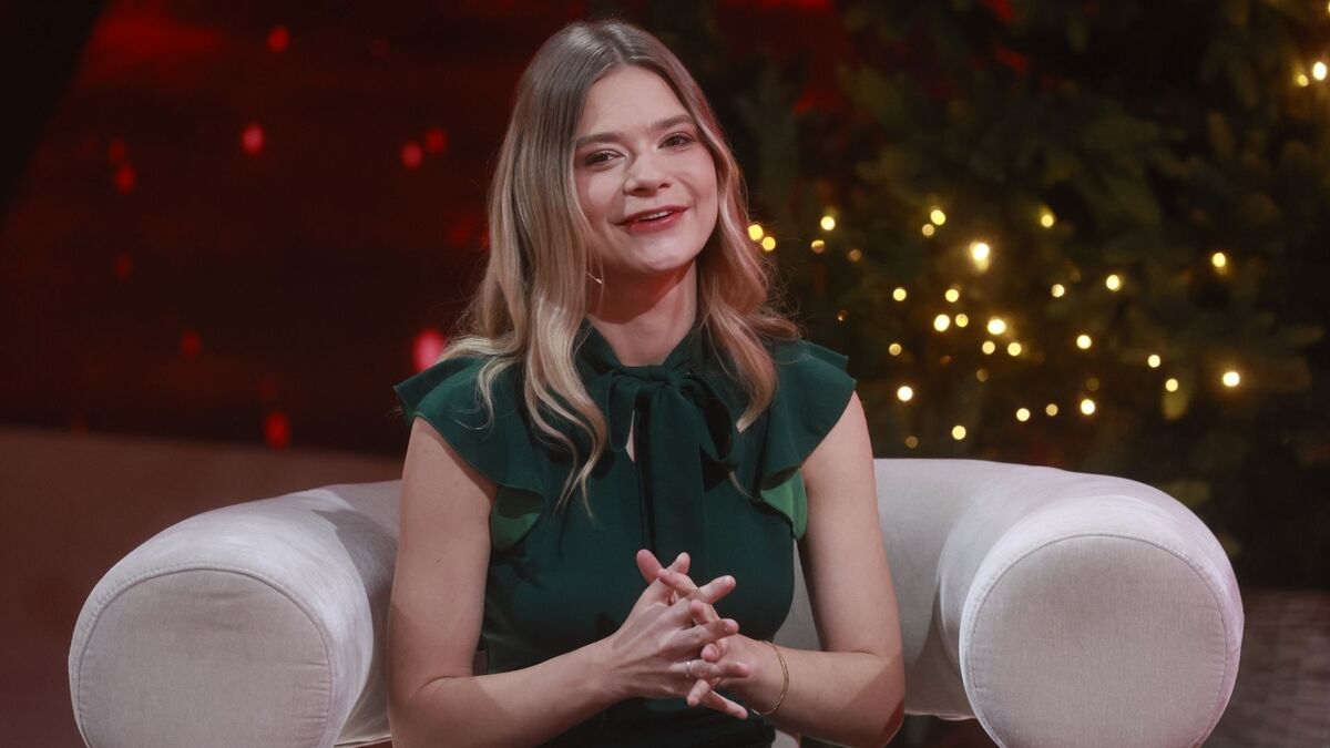 Julia Wróblewska w świątecznej aranżacji studia uśmiecha się do widzów, siedząc w jasnym fotelu. Ciepłe światła choinki w tle budują przytulny, bożonarodzeniowy klimat. Kadr pochodzi z programu „Pytanie na śniadanie”.